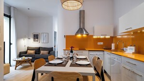 A modern kitchen with white cabinets, a stainless steel range hood, and a dining area with a table set for four. - Verdi 12 - Habitat Apartments (Barcelona)