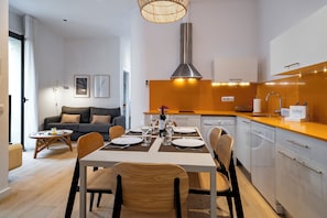 A modern kitchen with white cabinets, a stainless steel range hood, and a dining area with a table set for four. - Verdi 12 - Habitat Apartments (Barcelona)