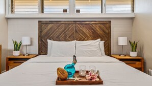 Ein ordentlich bezogenes Bett mit weißen Leinentüchern, einem Holz-Kopfteil und einem Tablett mit einer Flasche, Gläsern, einem Seestern und einer Pflanze auf einem Nachttisch aus Holz.