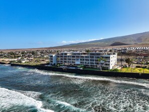 Un hotel costero con varios pisos, una zona de piscina y vistas al océano y colinas distantes.