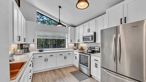 A modern kitchen with white cabinetry, stainless steel appliances, and a large window providing natural light. - Tahoe Retreat | Private Hot Tub & Scenic Views (Incline Village)