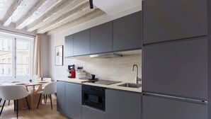 A modern kitchen with grey cabinets, a stainless steel refrigerator, and a built-in oven. - Charmant Appartement Climatisé - Marais (Paris)