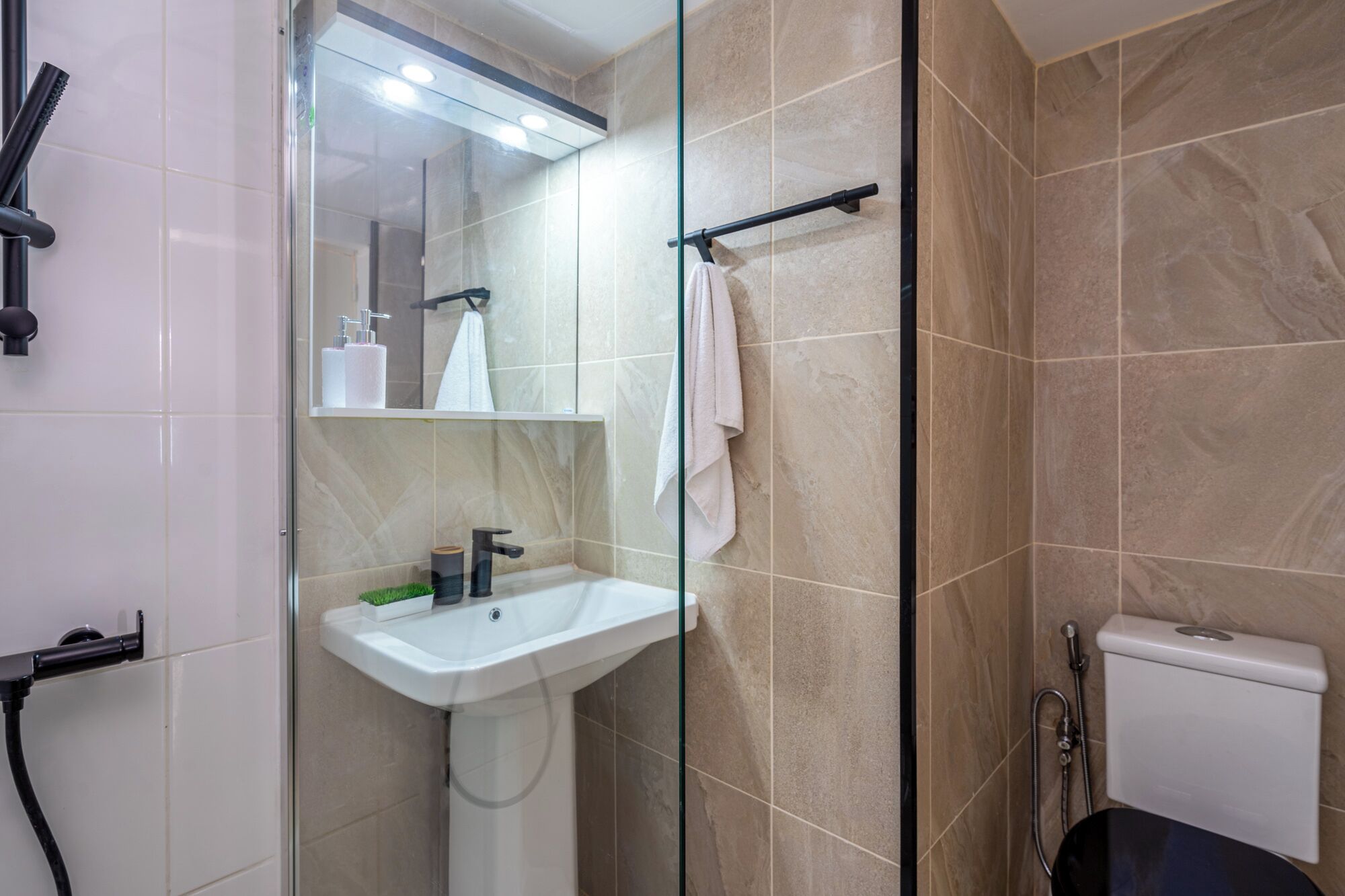 Een moderne badkamer met een douchecabine van glas, een witte wastafel en een toilet.