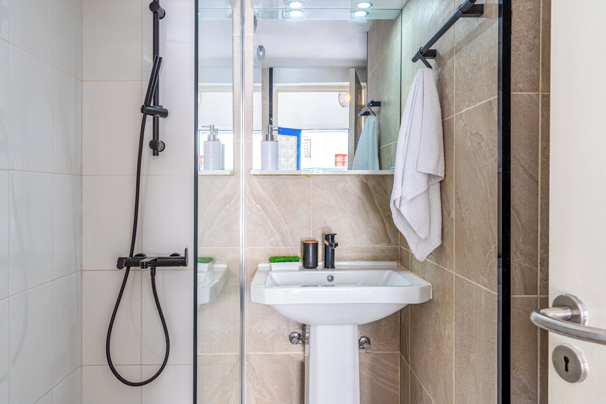Un baño moderno con cabina de ducha de vidrio, un lavamanos blanco sobre pedestal y un perchero.