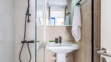 Un baño moderno con cabina de ducha de vidrio, un lavamanos blanco sobre pedestal y un perchero.