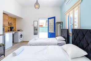 A modern hotel room with two beds, a kitchenette, a washing machine, and a view of the outside.