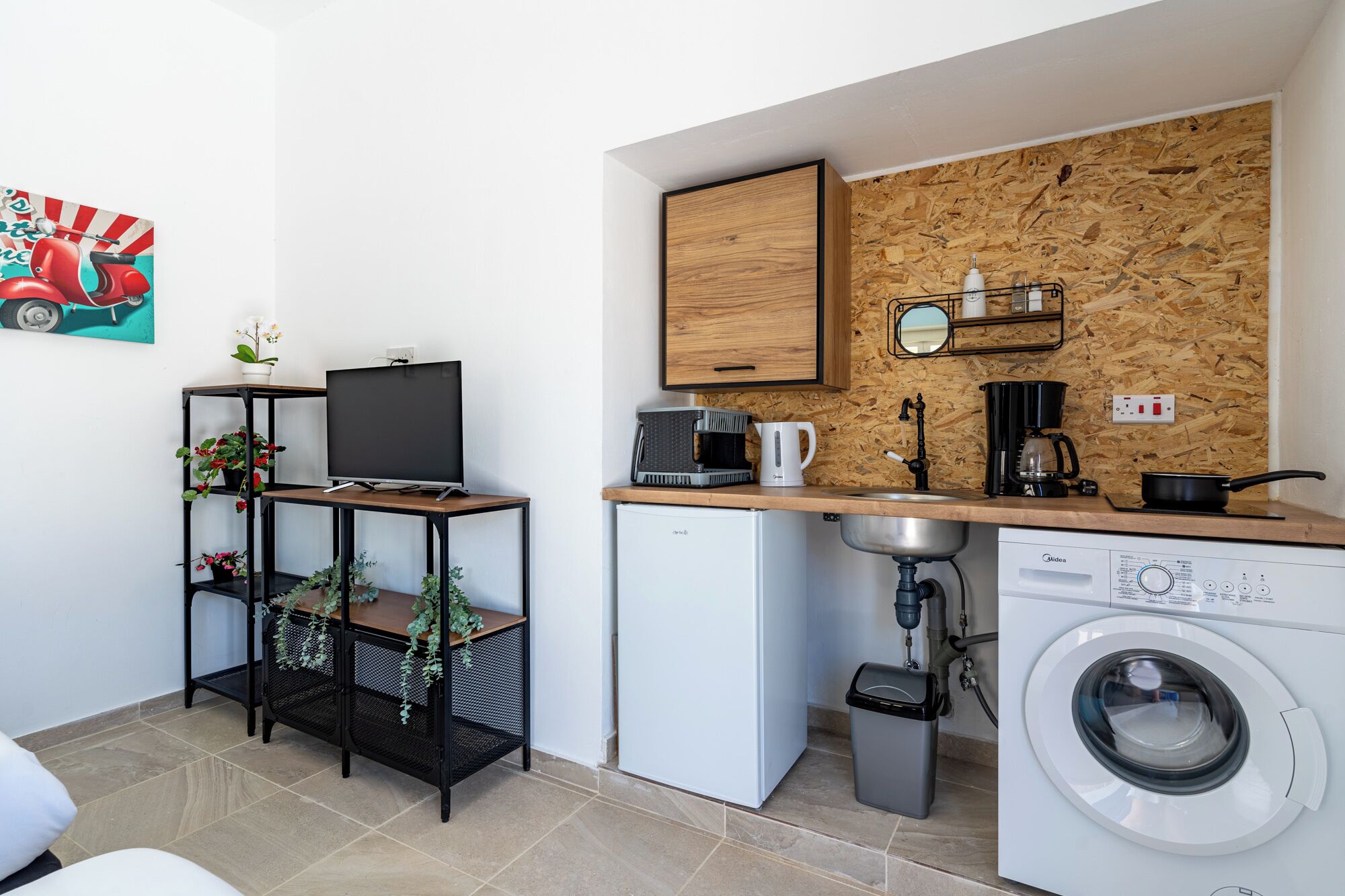 Cocina compacta con salpicadero de madera, cafetera, microondas y lavadora.
