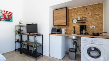 Cocina compacta con salpicadero de madera, cafetera, microondas y lavadora.