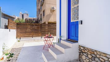 Una pequeña zona de estar al aire libre con una mesa y sillas, una puerta azul y un muro de piedra.