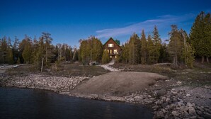 A cabin with a dirt path leading to a wooden dock over a rocky riverbank.