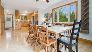 A spacious kitchen with wooden cabinets, a dining table, and chairs, a ceiling fan, and large windows.