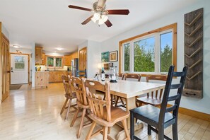 A spacious kitchen with wooden cabinets, a dining table, and chairs, a ceiling fan, and large windows. - Paradise Pines | Waterfront | Beach + Dock (Miller Lake)