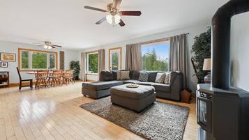 A spacious living room with a large sofa, a dining table with chairs, a ceiling fan, and a fireplace.
