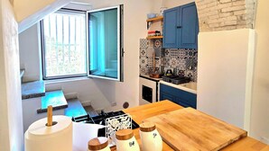 A kitchen with a wooden table, a hanging light fixture, and a view of the dining area through an open window.