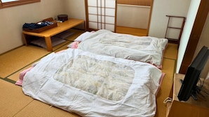 Een traditionele Japanse kamer met tatami vloerbedekking, twee tatami matten, een houten bank, een futon bed en een televisietoestel.