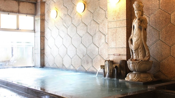 Een stenen muur met hexagonale patronen, een beeld en een waterpartij.