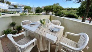 En balkon med et bord dækket til to, omgivet af hvide stole med mønstrede puder, plantekasser og et frit udsyn til det omkringliggende landskab.