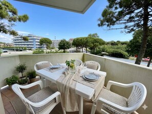 A balcony with a table set for two, surrounded by white chairs with patterned cushions, potted plants, and a clear view of the surrounding area. - Spacious beachside flat with terrace (Porto Santa Margherita)