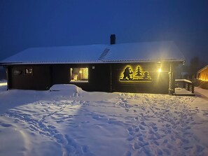 A snow-covered building with a wooden exterior and a lit-up silhouette of a bear and a dog on the wall.