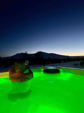 A person in a green-lit pool at dusk with a mountain in the background.