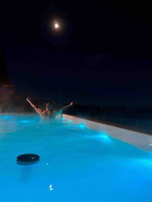 Une personne se détend dans une piscine chauffée la nuit, avec la lune en arrière-plan.