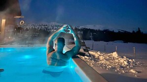 A person in a hot tub outdoors at night with a snowy mountain in the background.