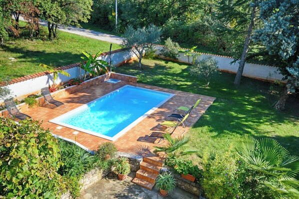 A rectangular swimming pool with a tiled deck, surrounded by a garden with various plants and a brick wall. - Flat with pool close to Kanegra Beach (Valica)