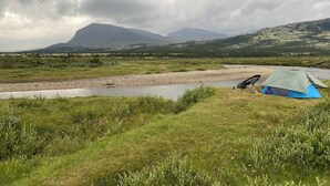 Una tenda montata vicino a un fiume, con montagne sullo sfondo.