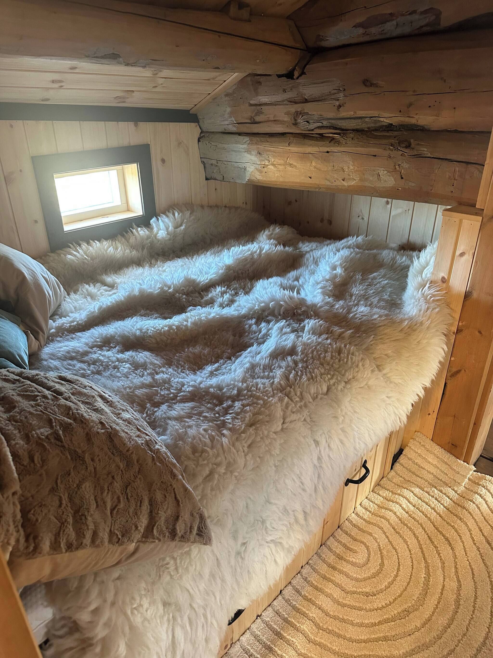 A cozy room with a large bed covered in fluffy white bedding, wooden walls, and a small skylight.