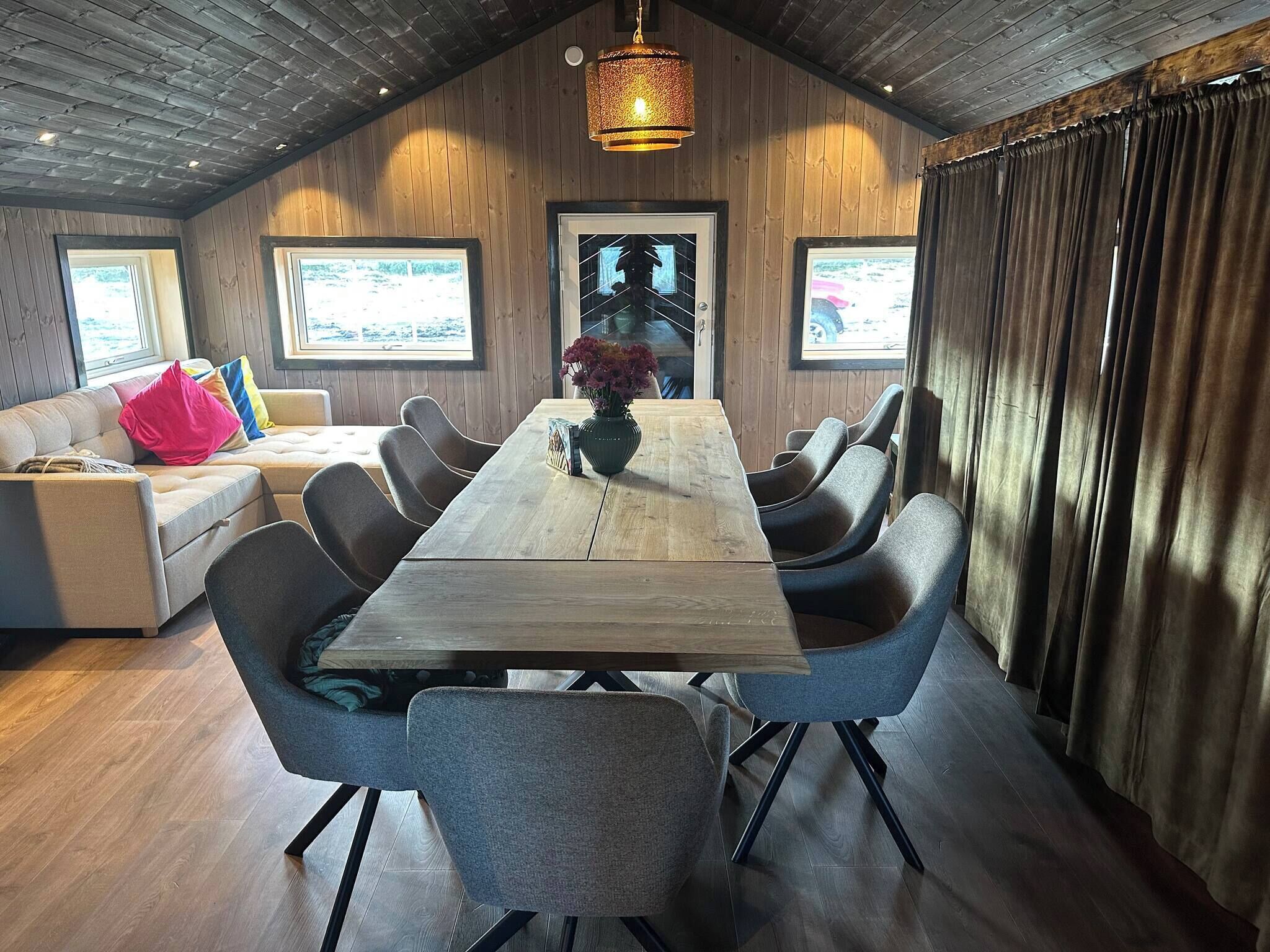 A dining area with a long wooden table, grey upholstered chairs, and a vase with flowers.