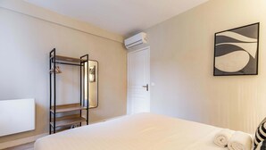 Habitación de hotel con cama, armario con ropa colgada, equipo de aire acondicionado y una obra de arte en la pared.