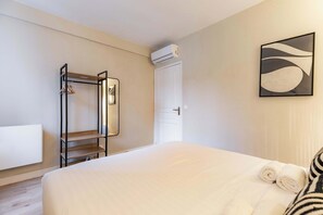 Ein Hotelzimmer mit Bett, einem Kleiderschrank mit Kleidung und einer Klimaanlage, sowie einem Wandbild.