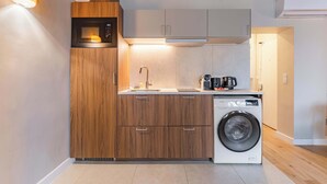 Cocina compacta con armarios de madera, microondas integrado, pileta y lavadora de carga frontal.