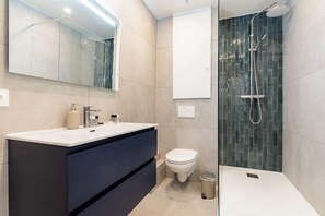 Ein modernes Badezimmer mit einem großen Spiegel, einem Waschbecken, einer Toilette und einer Dusche.