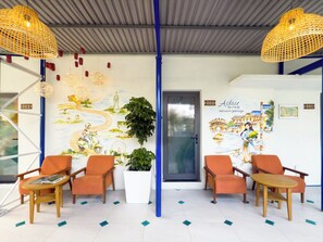 Zona de recepción con sillas color naranja, una planta grande en maceta y un mural que representa un viaje.