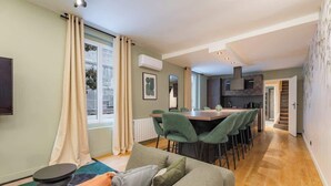 A modern living room with a sofa, dining area with chairs, and a kitchen in the background. - Triplex d'exception 150m2 - 6BR (Paris)