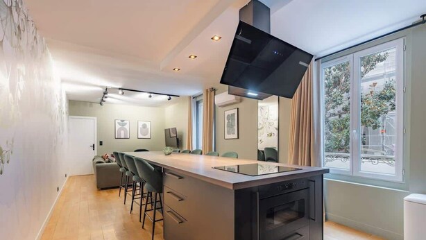 A modern kitchen with a central island, built-in oven, and a large window providing a view of the outdoors. - Triplex d'exception 150m2 - 6BR (Paris)