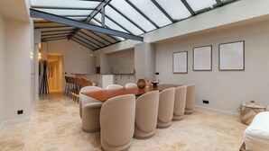 A spacious dining area with a high ceiling and skylight, a long wooden table, and several cushioned chairs. - Splendeur de 187m² Climatisé au Cœur de Paris (Paris)