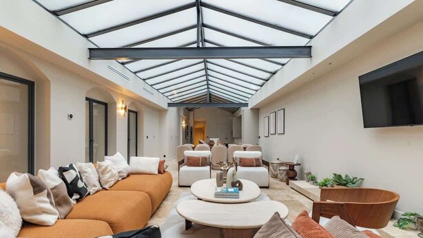 A spacious living area with a high ceiling and skylight, furnished with sofas, a coffee table, and a TV mounted on the wall. - Splendeur de 187m² Climatisé au Cœur de Paris (Paris)