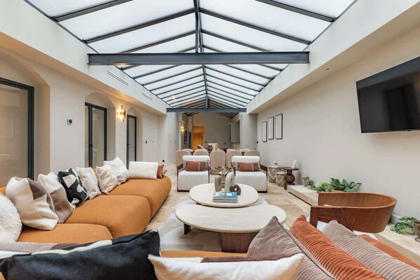 Ein großzügiger Wohnbereich mit hohen Decken und Oberlichter, ausgestattet mit Sofas, einem Couchtisch und einem an der Wand befestigten Fernseher.