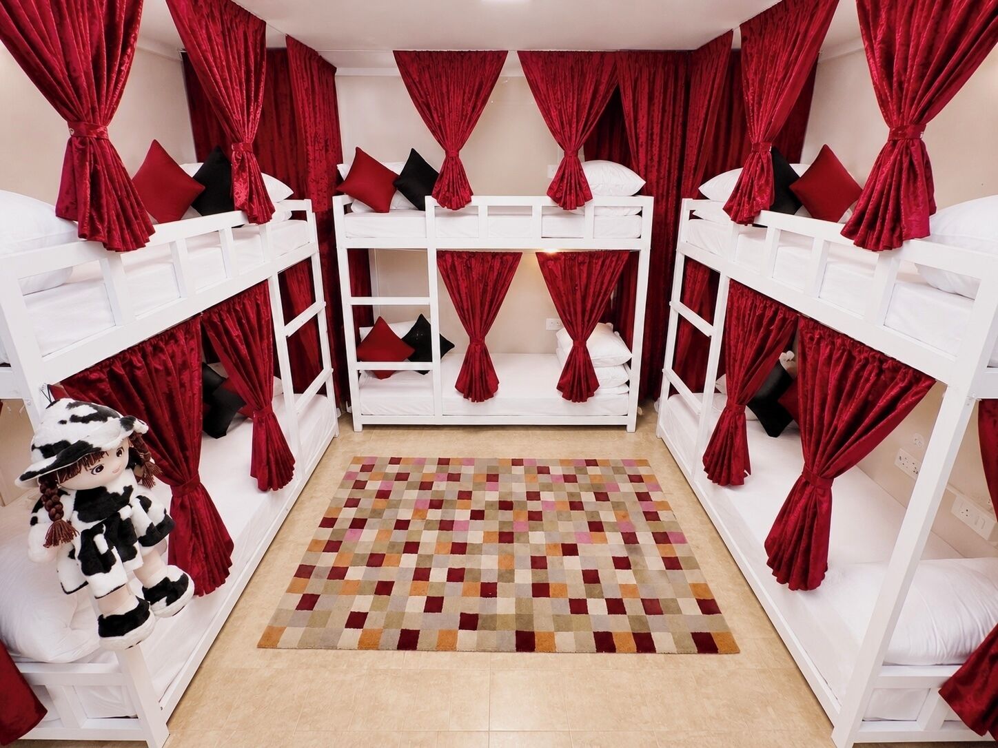 A room with bunk beds, red curtains, and a patterned rug.