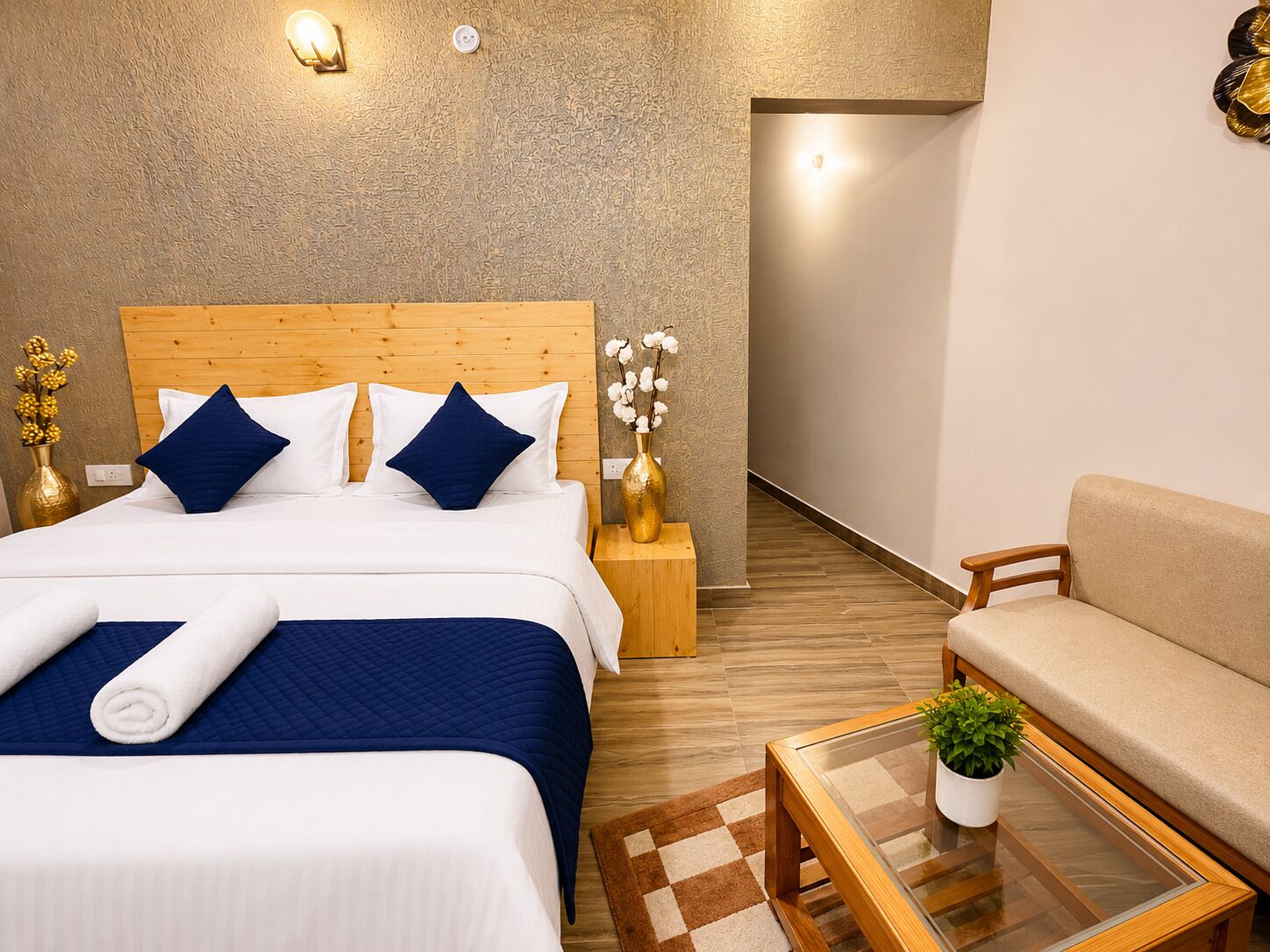 Une chambre d’hôtel avec un lit en bois, un canapé, une table basse en verre et une petite plante en pot.