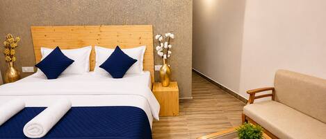 Une chambre d’hôtel avec un lit en bois, un canapé, une table basse en verre et une petite plante en pot.