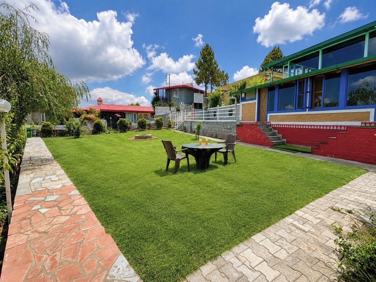 A well-maintained lawn with a stone pathway, a small table with chairs, and a building with large windows and a red and blue exterior.