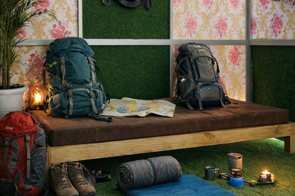 A room with a bed, two backpacks, a map, a Buddha head sculpture, a small Buddha statue, a doll, a plant, and camping gear.