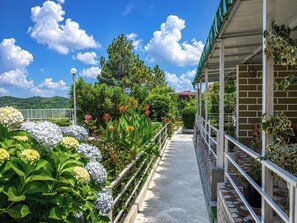 A pathway flanked by lush greenery and flowers, leading to a building with a covered porch and a brick wall. - Five Hill Cottage Mukteshwar (Mukteshwar)