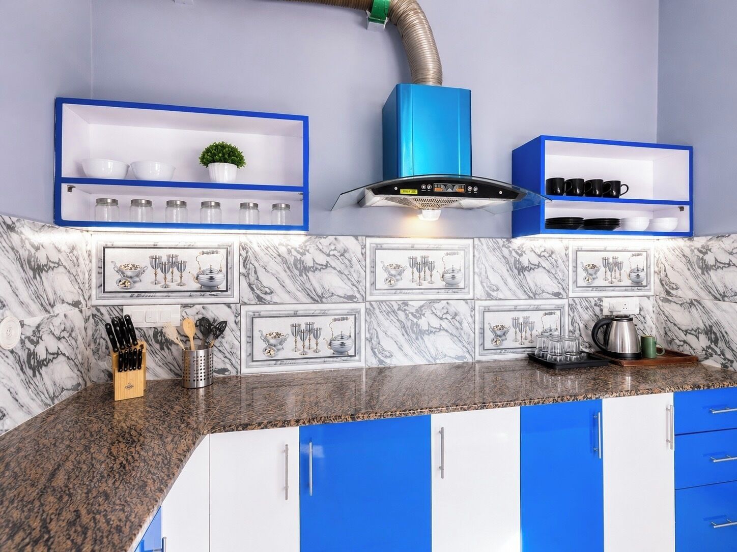 Una cocina con armarios azul y blanco, salpicadero de mármol y campana extractora.