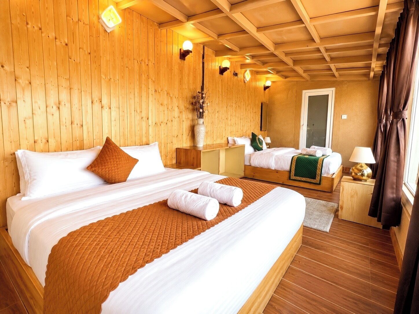 A wooden-paneled room with a large bed, a bedside table, a mirror, and a window with curtains.