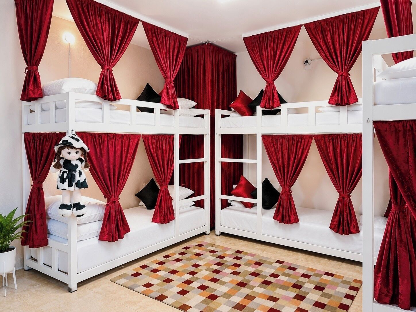 A room with two bunk beds, red curtains, a checkered floor, and a doll on the left bed.