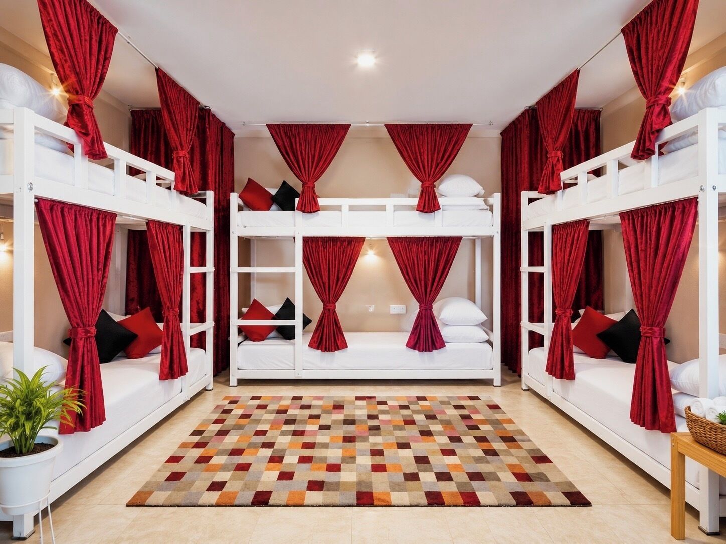 Ein Zimmer mit Etagenbetten, roten Vorhängen, einem gemusterten Teppich und einer Topfpflanze.
